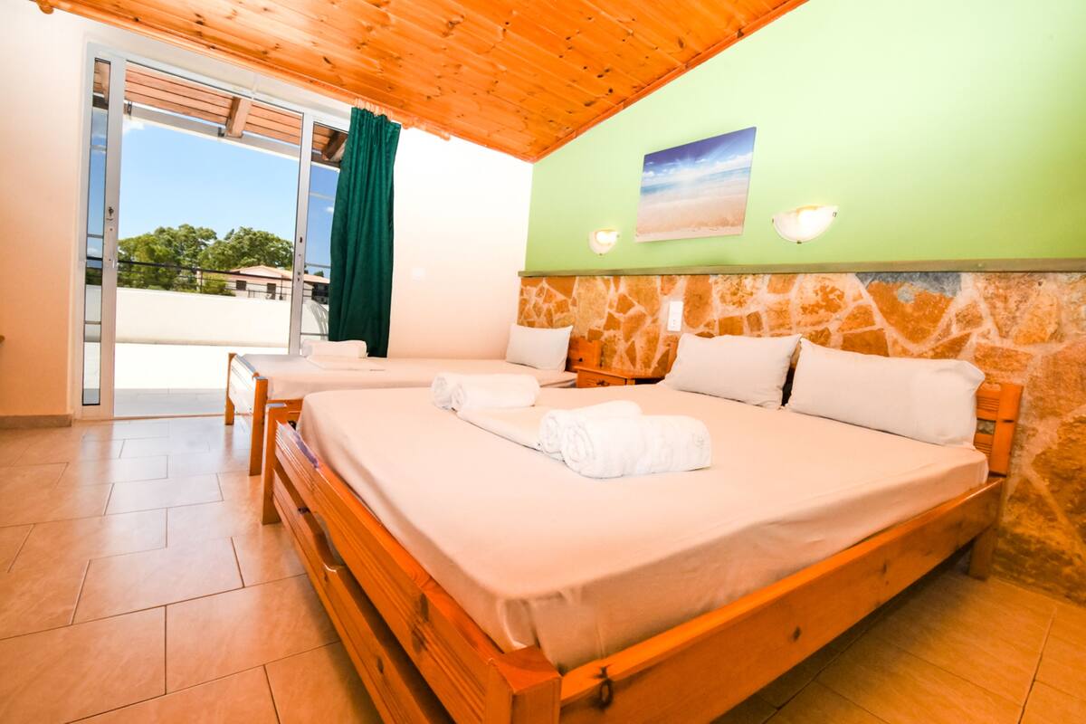 A room with two beds, wooden headboards, a stone wall, and a view through a glass door.