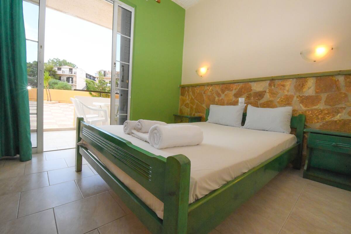 A room with a bed, a green wall, a stone accent wall, and a view through a glass door.