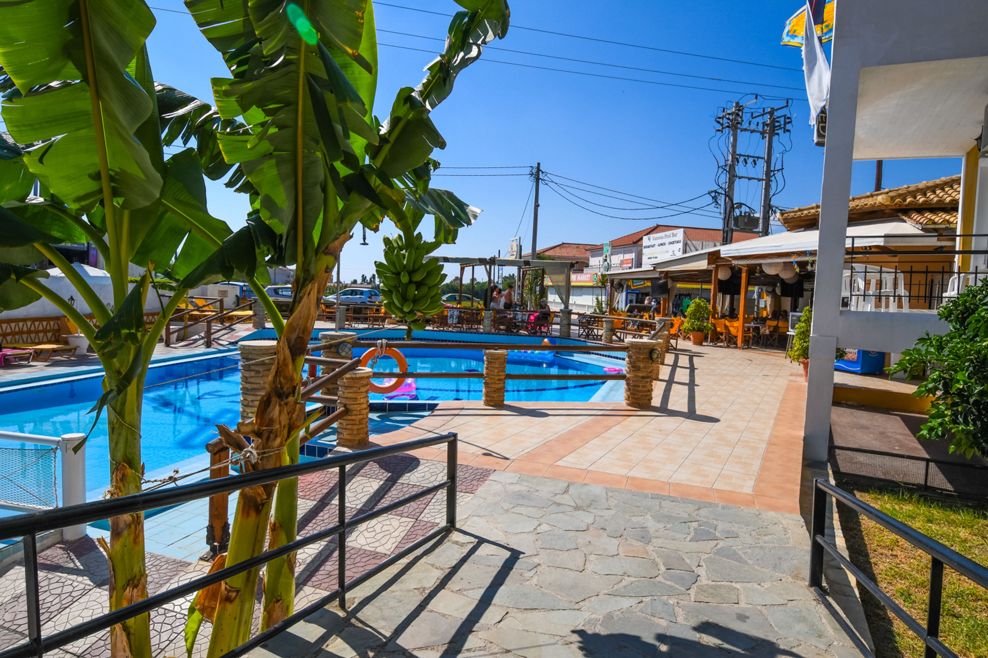 A swimming pool area with a tiled deck, surrounded by palm trees and outdoor seating.