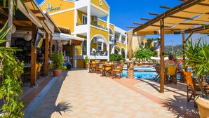A hotel with outdoor seating, a pool, and a yellow building with a sign. - Vanessa Hotel (Zakynthos)