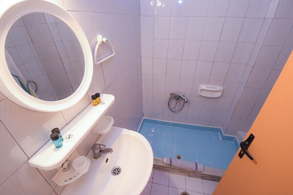 A bathroom with a white sink, a mirror, a toilet, and a blue shower area. - Vanessa Hotel (Zakynthos)