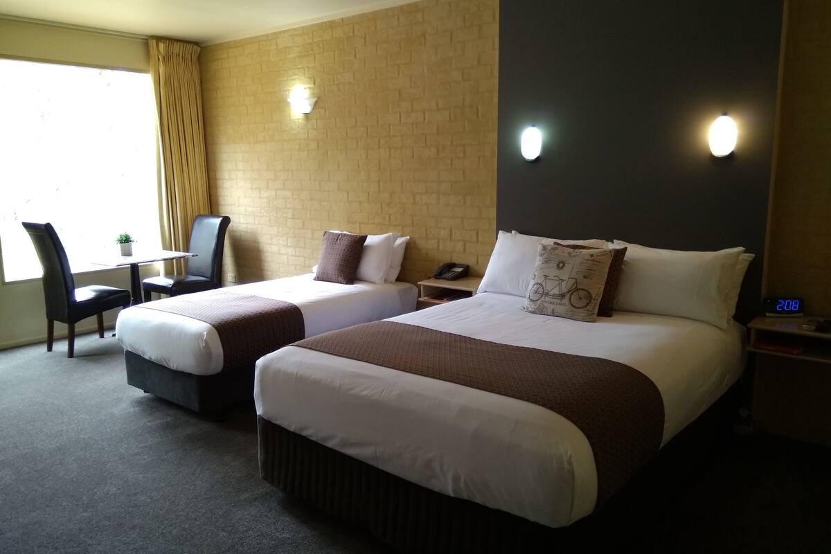 A hotel room with two beds, a desk, a chair, and a small table with a plant.