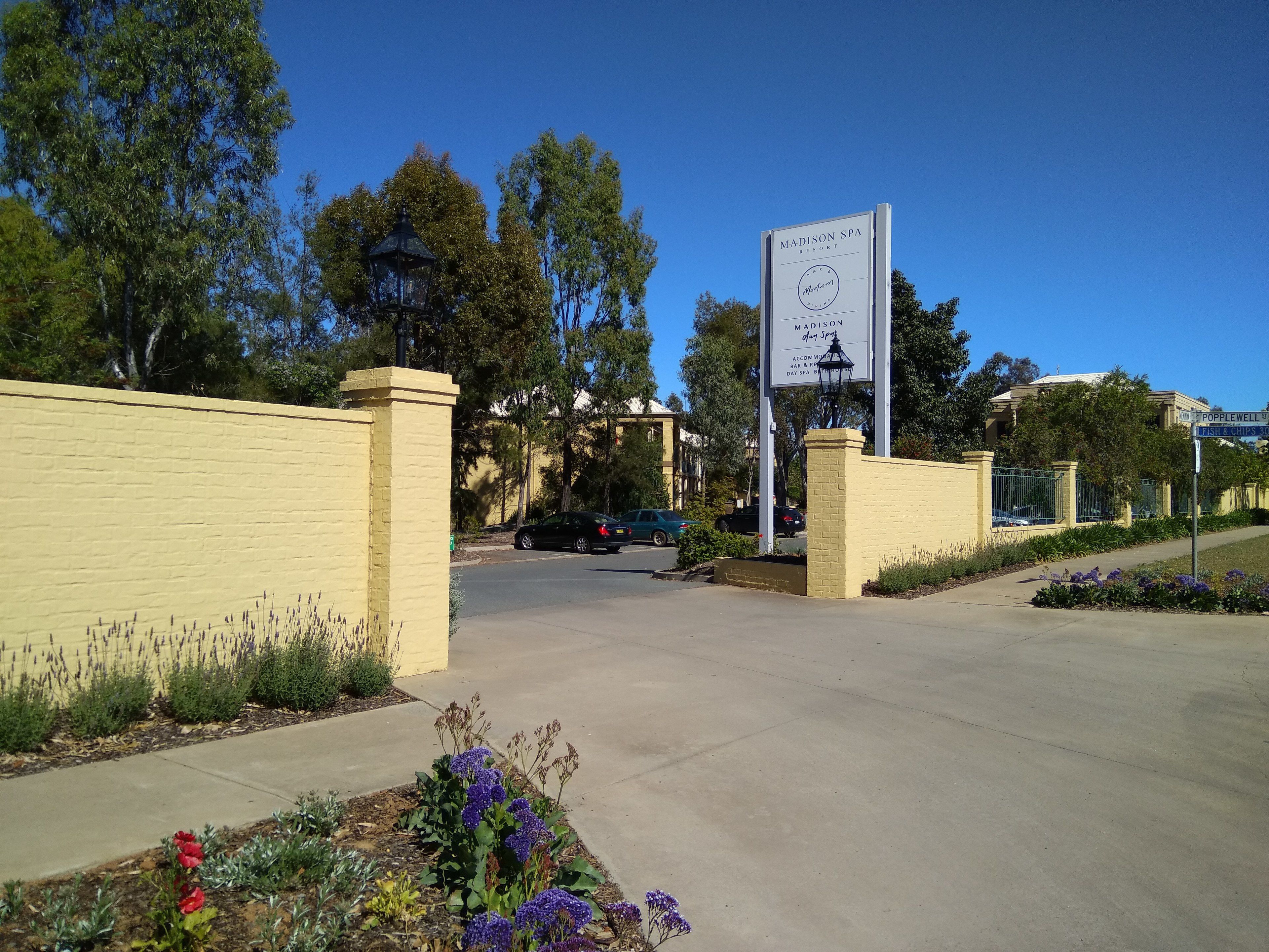 Señal del Madison Spa Resort con entrada despejada, camino pavimentado y follaje circundante.