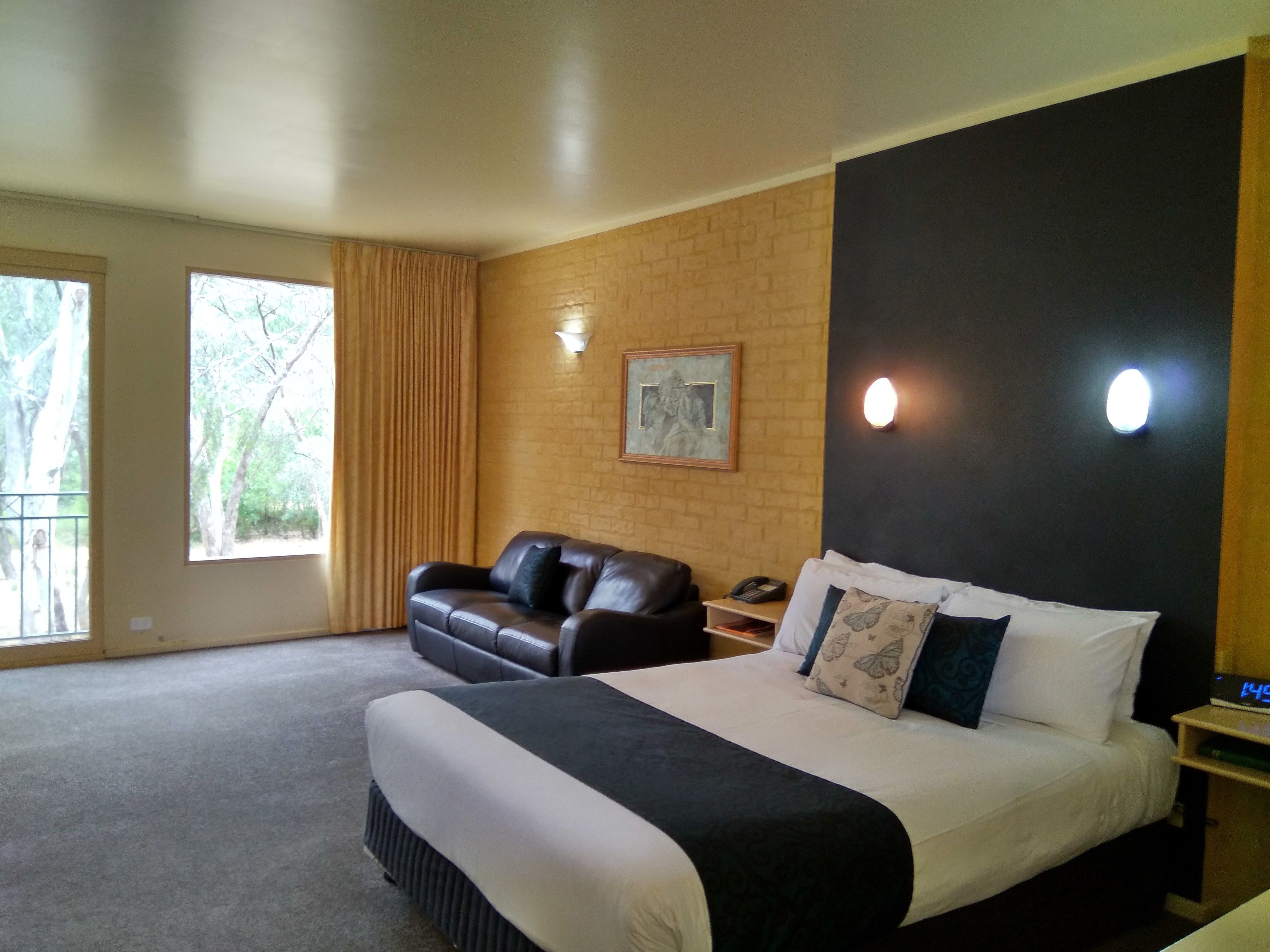A bedroom with a large bed, a leather sofa, a desk with a telephone, and a window with curtains.