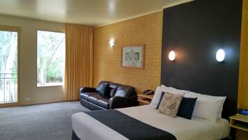 A bedroom with a large bed, a leather sofa, a desk with a telephone, and a window with curtains.