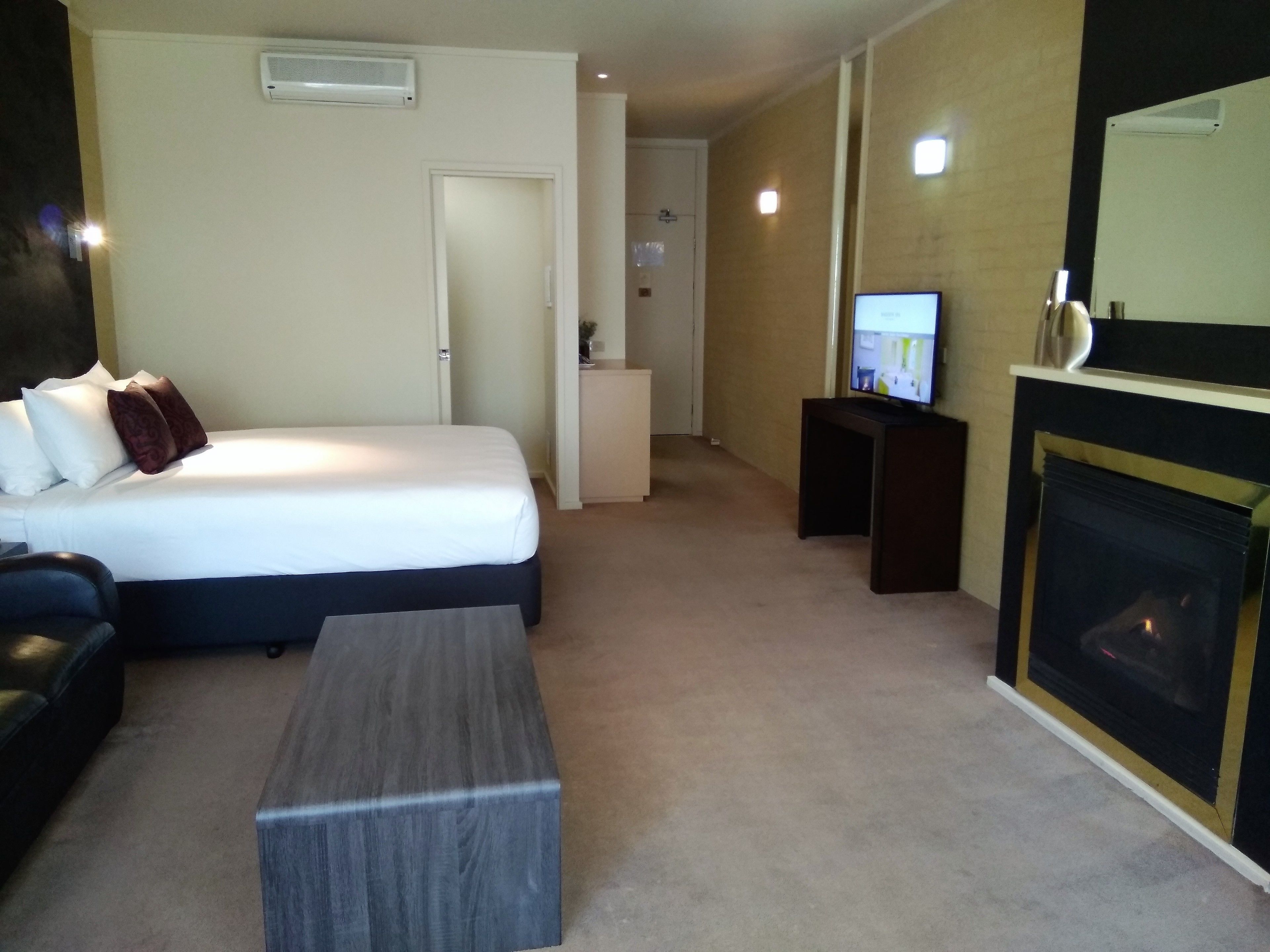 A hotel room with a bed, a TV, a fireplace, and a desk.