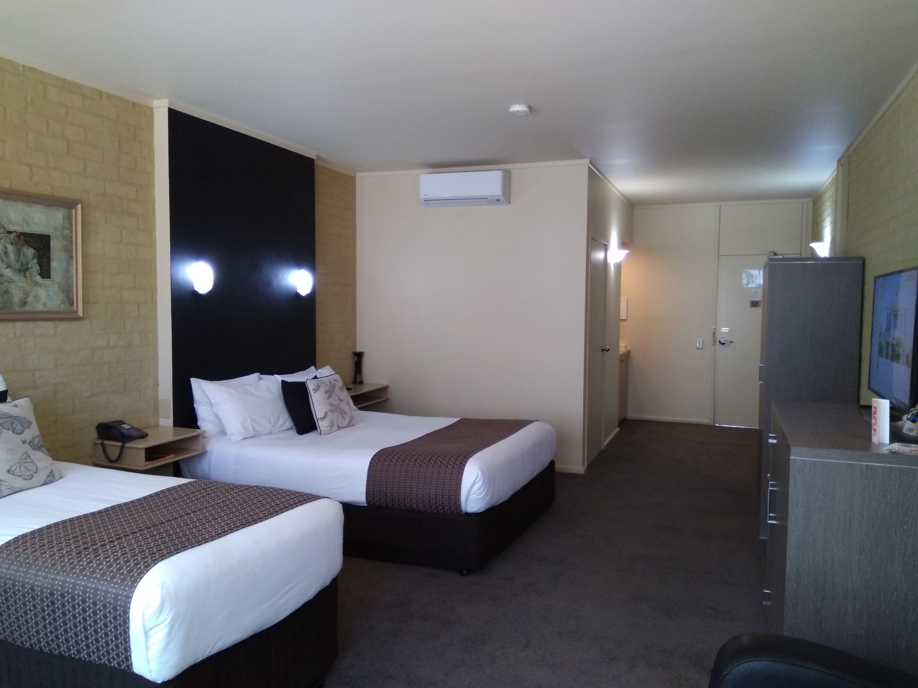 Quarto de hotel com duas camas, uma escrivaninha com telefone, ar condicionado, televisão e porta de acesso a um banheiro.