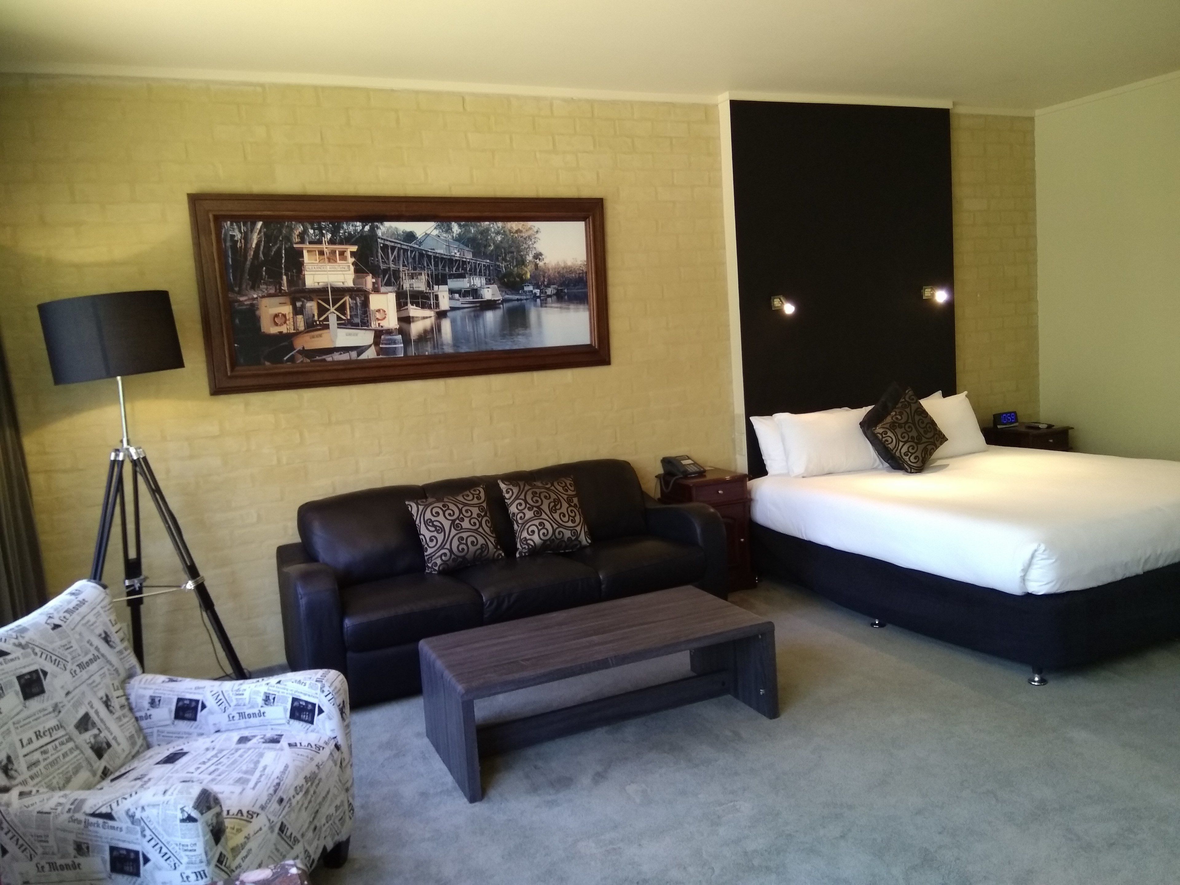 Habitación de hotel con cama, sofá, mesa de centro, lámpara y un cuadro en la pared.
