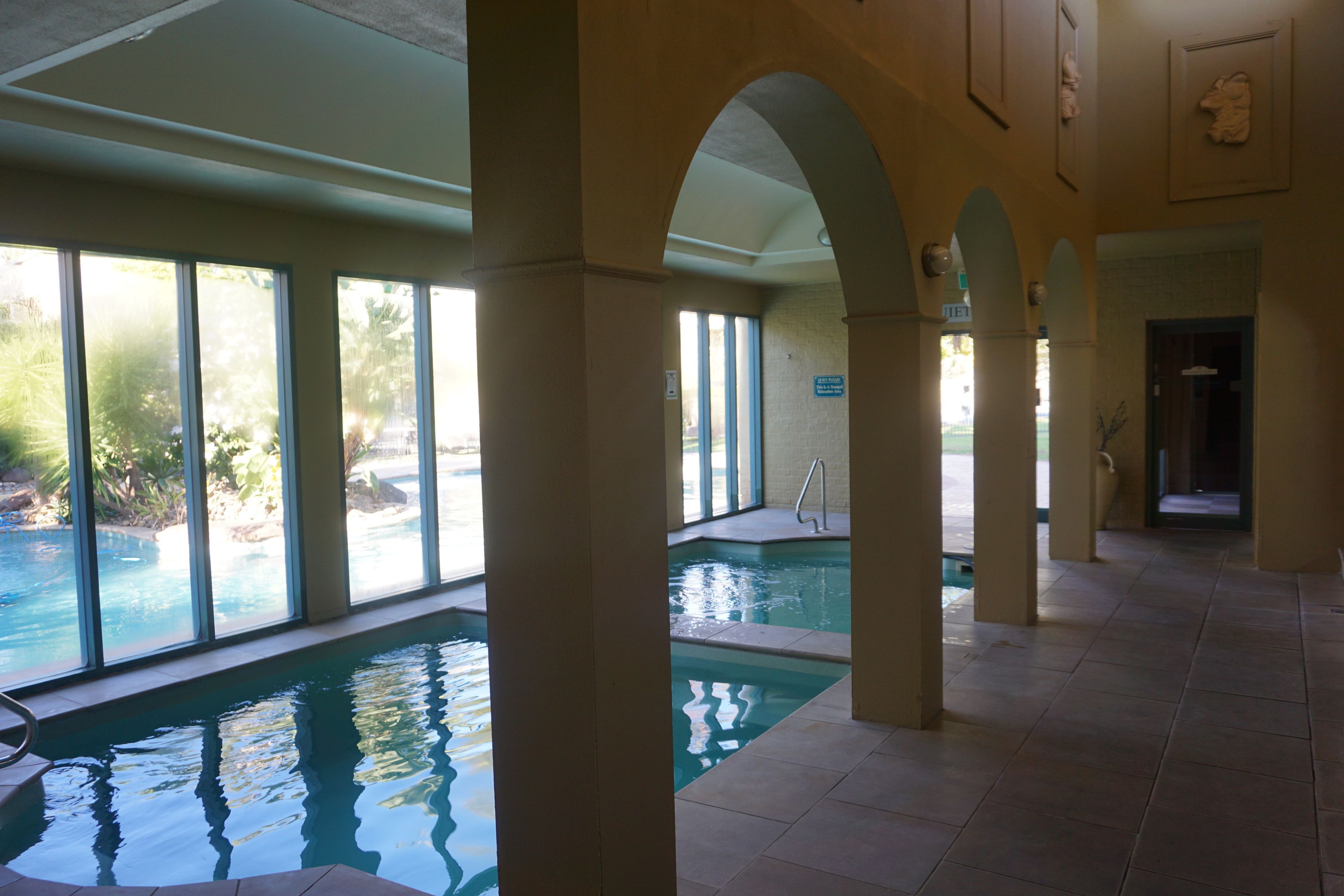 An indoor swimming pool with clear glass walls, a tiled floor, and a view of the outdoors.