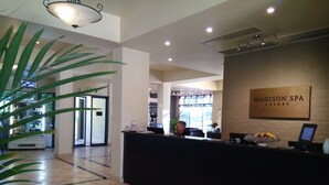 Un área de recepción con mostrador, un cartel que dice 'Madison Spa Resort' y una planta a la izquierda.