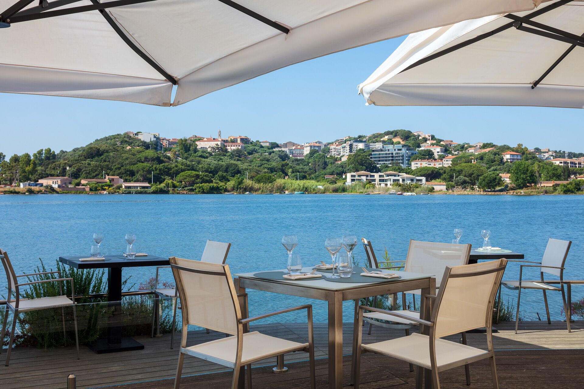 Zona pranzo sul lungolago con tavoli e sedie, affacciata su un lago con edifici sullo sfondo.