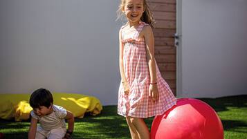 Children can play freely in the lush grassy area surrounded by tall palm trees.