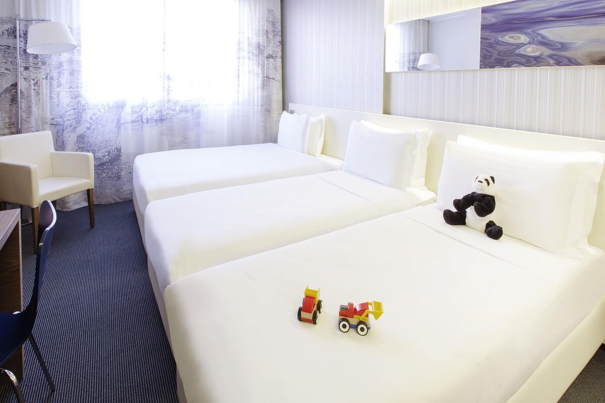 A hotel room with two beds, a desk, a chair, and a panda plush toy on one of the beds.