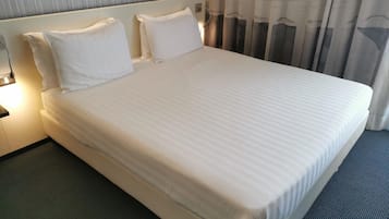 A hotel room with a large bed, two pillows, a nightstand with a lamp, and a window with curtains.