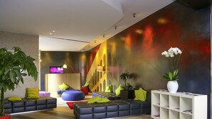Un hall d’entrée moderne comprenant un comptoir d’accueil, des espaces de détente et une fresque murale aux couleurs vives.