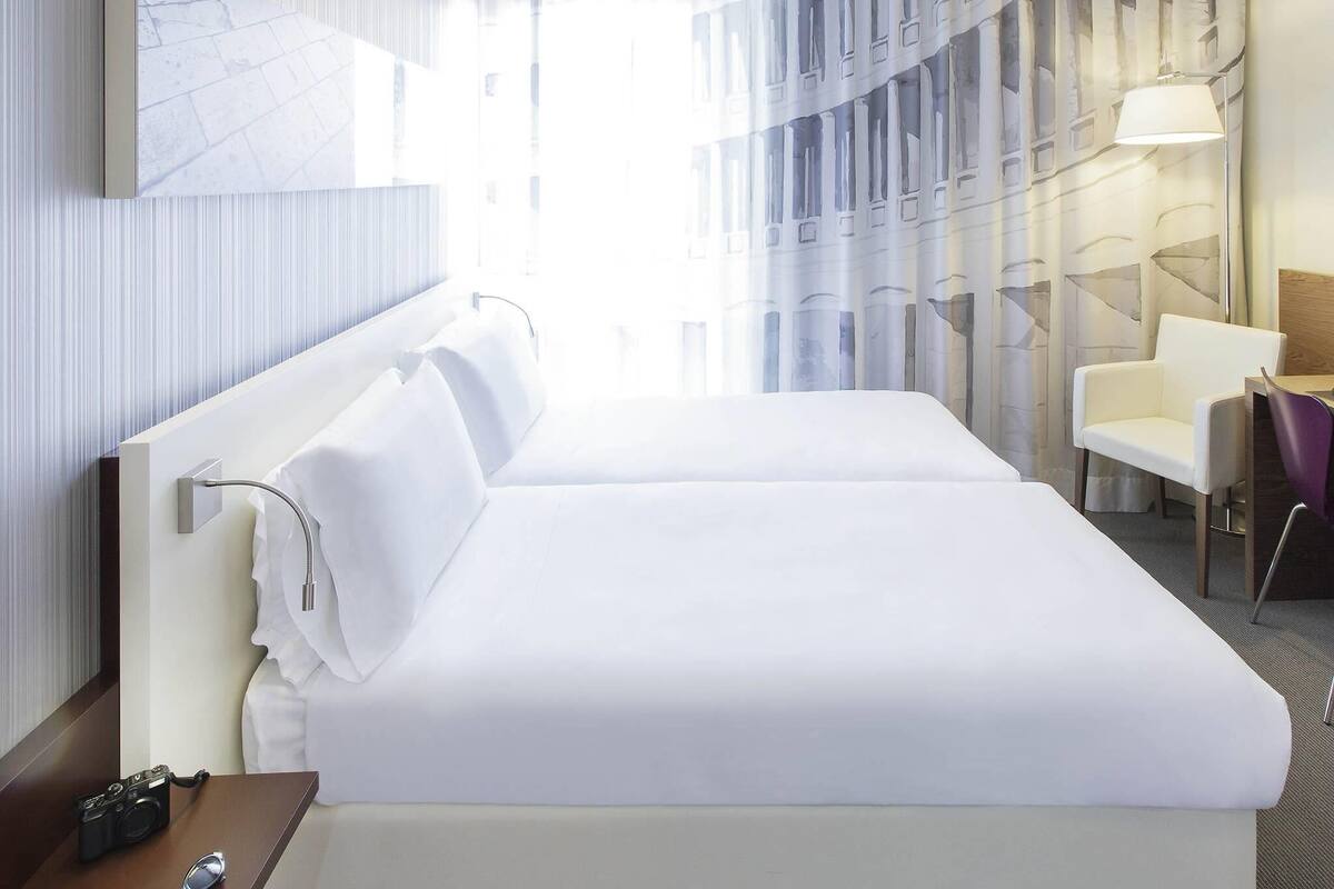 Een hotelkamer met twee bedden, een bureau, een stoel, een lamp en een camera op het nachtkastje.