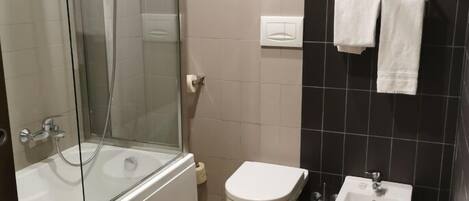 A modern bathroom with a glass-enclosed shower, a bathtub, a toilet, a bidet, and a towel rack.