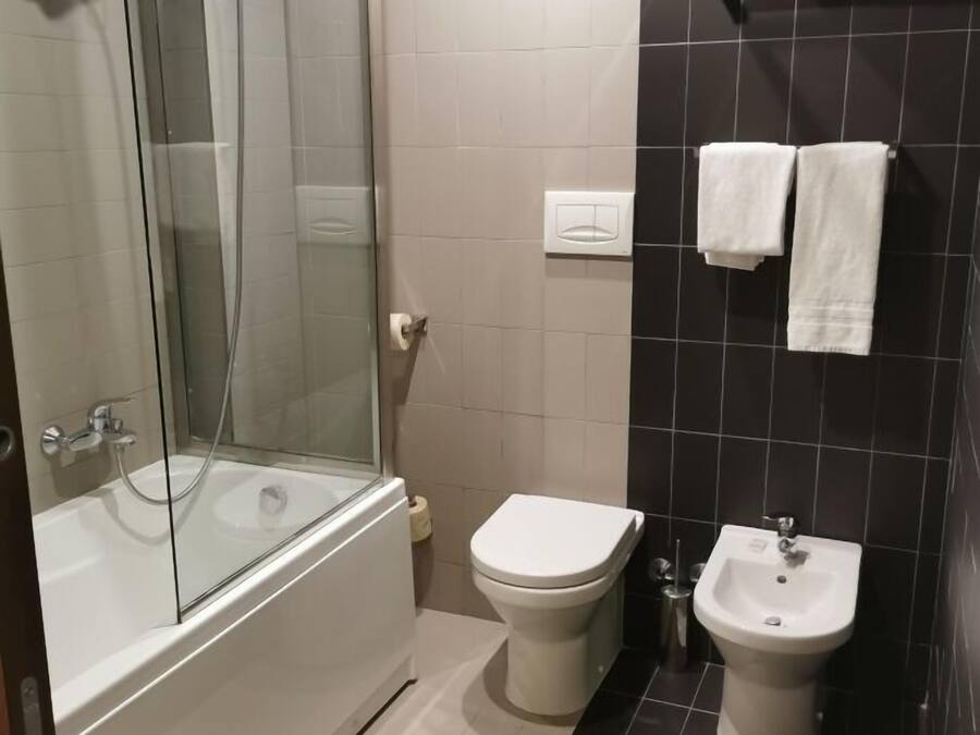 A modern bathroom with a glass-enclosed shower, a bathtub, a toilet, a bidet, and a towel rack.