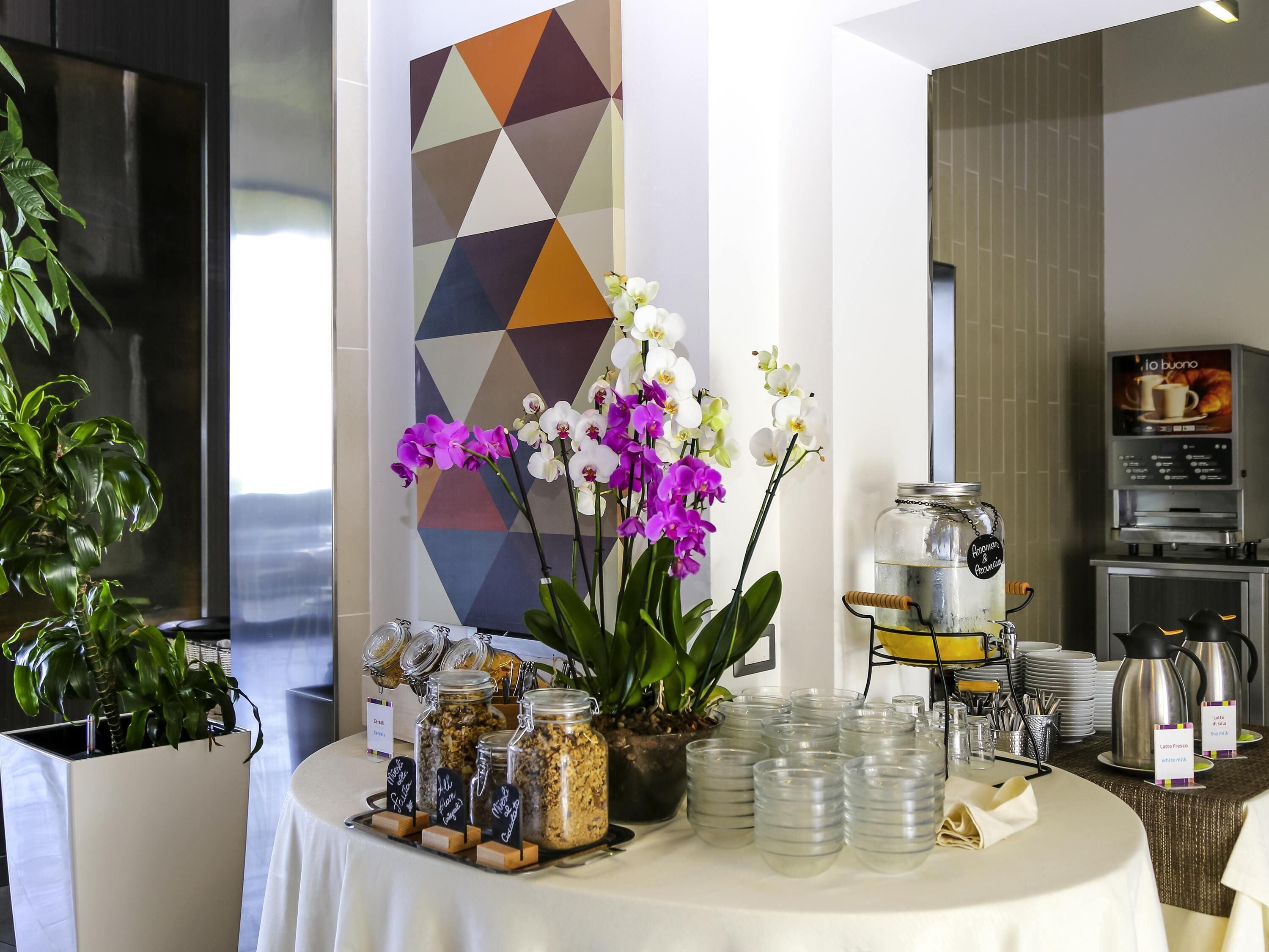 A breakfast buffet with jars of spreads, a coffee machine, and a decorative wall.