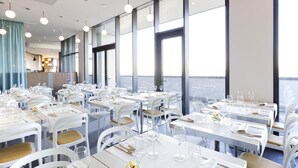 Un restaurant moderne avec des tables et des chaises blanches, de grandes fenêtres et des lampes suspendues.