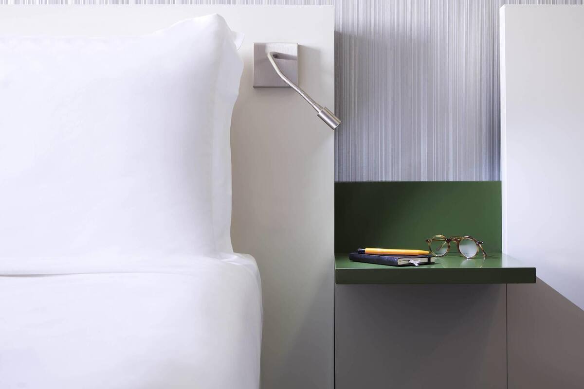 Een moderne kamer met een wit bed, een groen nachtkastje met glazen en een boek, en behang met strepen.