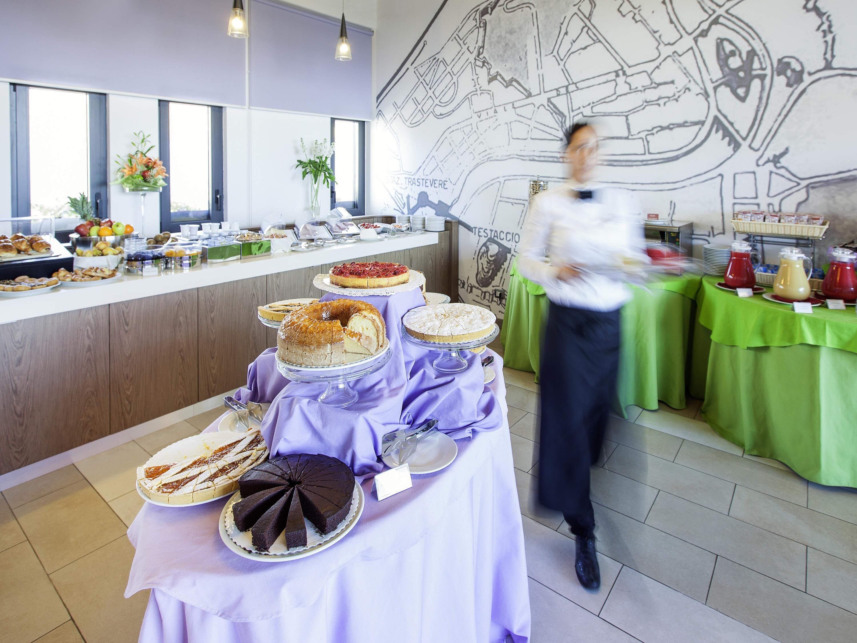 A buffet setup with various cakes and pastries on a table, a person in the background, and a wall with a map.