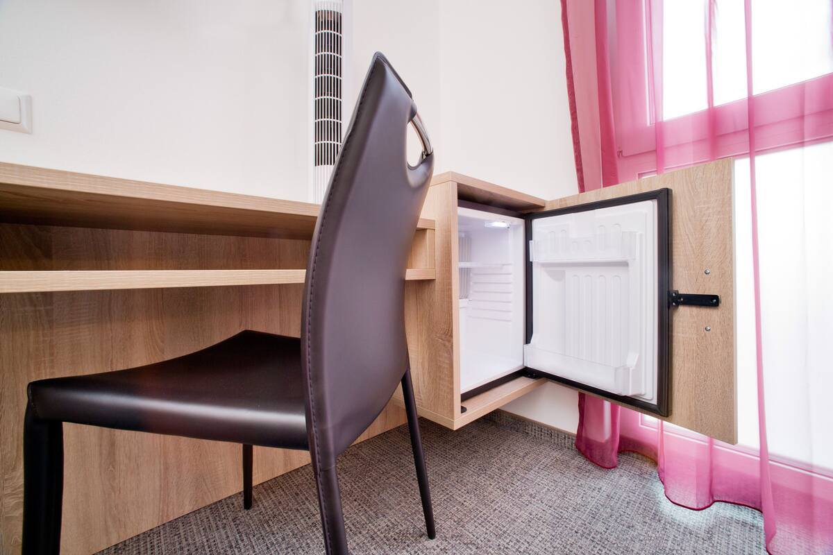 A room with a wooden desk, a black chair, and a window with pink curtains.