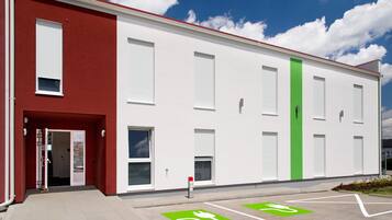 A modern building with a red and white facade, large windows, and designated parking spaces for electric vehicles.