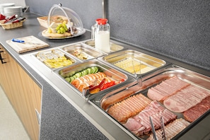 Un bufé con diversas opciones de comida, incluyendo carnes, quesos y frutas.