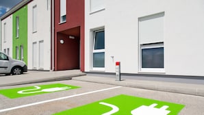 Un estacionamiento con estaciones de carga para vehículos eléctricos, señalizadas con cuadrados verdes y símbolos de enchufes blancos.