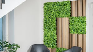 Un interior moderno con una escalera, dos sillas negras con cojines verdes, una mesita y una planta en maceta.