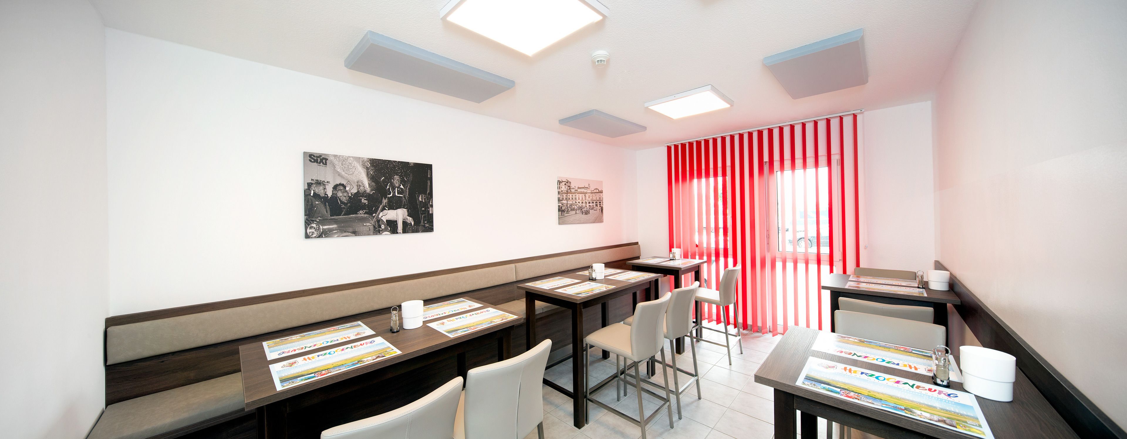 A modern hotel room with a long table, chairs, and a red curtain.