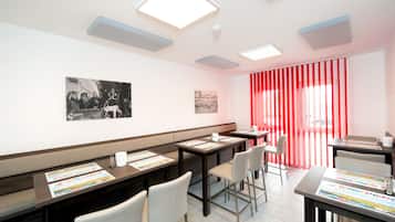 A modern hotel room with a long table, chairs, and a red curtain.