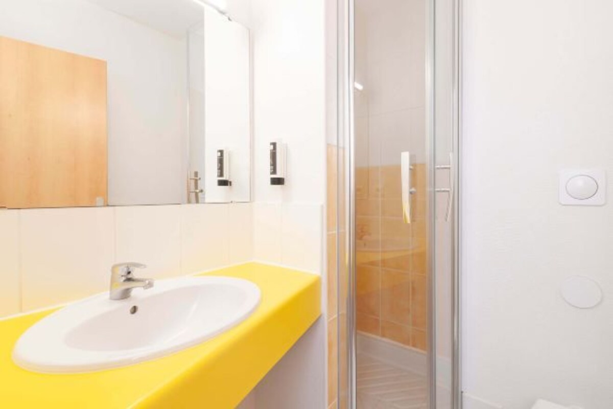Un baño moderno con un lavamanos amarillo, una cabina de ducha de vidrio y una pared con azulejos blancos.