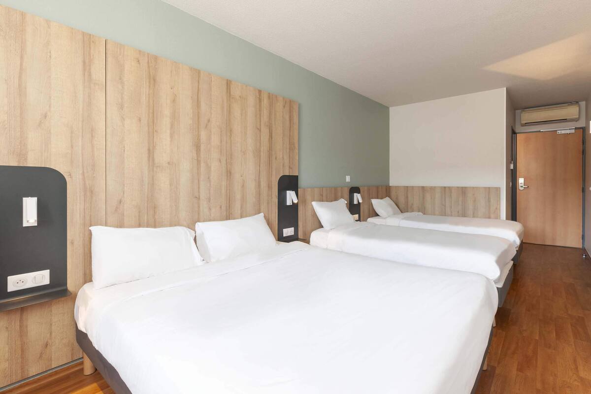 A hotel room with three beds, wooden paneling on the walls, a flat-screen TV, and a door with an air conditioning unit.