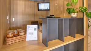 Un'area reception con scrivania in legno, una TV a schermo piatto montata a parete, una pianta in vaso e un cartello che descrive i servizi delle camere.