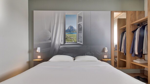 Una camera da letto con un'ampia finestra, un letto, lampade sui comodini e un'armadio in legno.