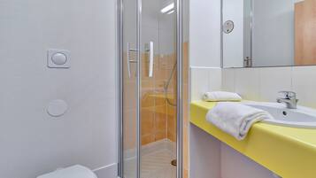 A bathroom with a glass-enclosed shower, a white toilet, a yellow sink with a white towel, and a mirror above the sink.