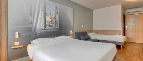 A modern hotel room with a large bed, a smaller bed, a window with a view of buildings, and an air conditioning unit.