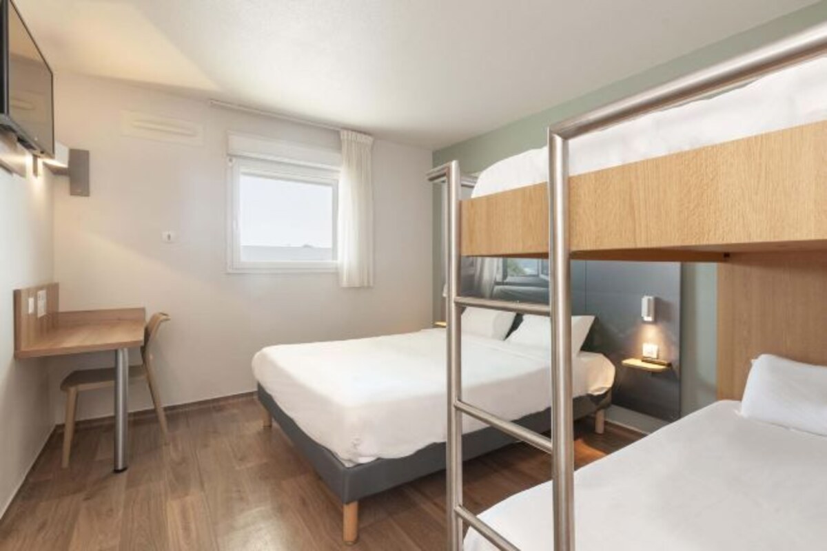 Una habitación de hotel compacta con literas, un escritorio y una mesita de noche con lámpara.