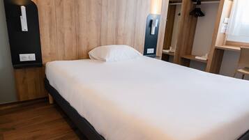A neatly made bed with a white mattress and pillow, a wooden headboard, and a black bedside table with a light switch.