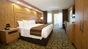 Une chambre d’hôtel avec un grand lit, une tête de lit en bois, une table de chevet avec une lampe, une armoire et une vue sur l’extérieur par la fenêtre.