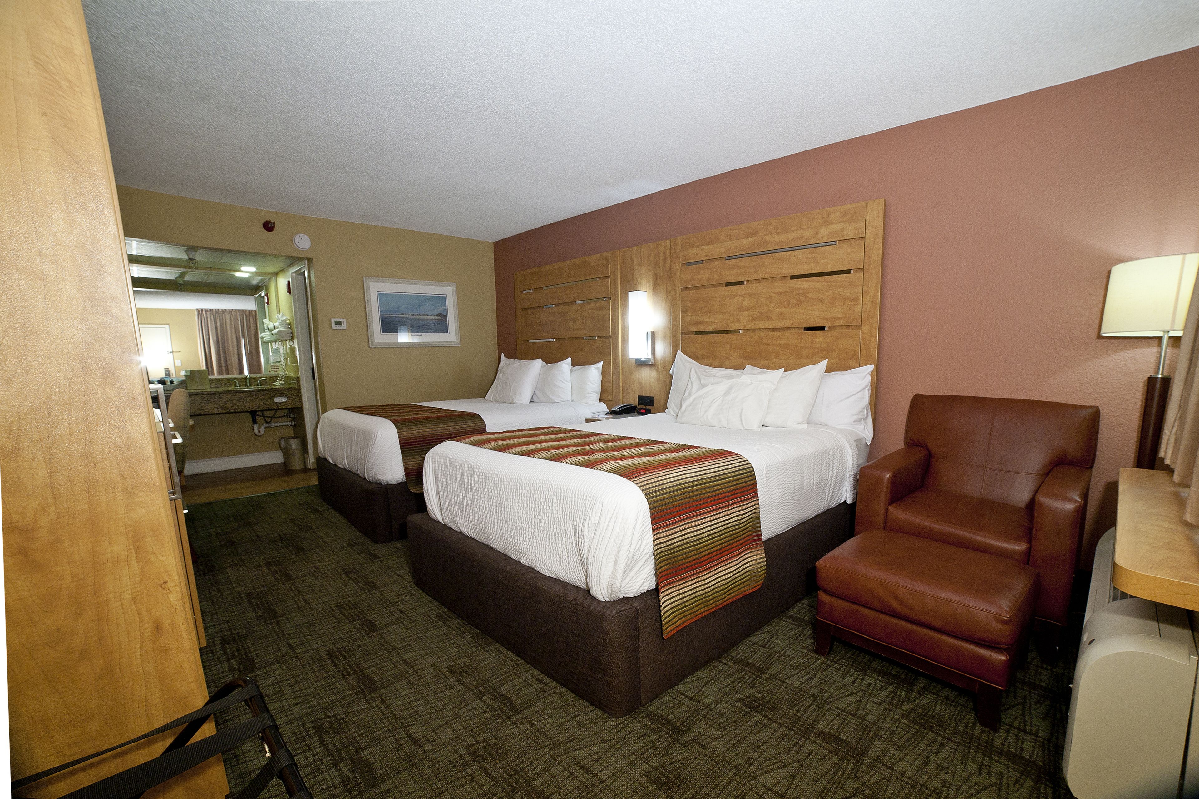 A hotel room with two beds, a brown leather armchair, a desk, and a mirror.