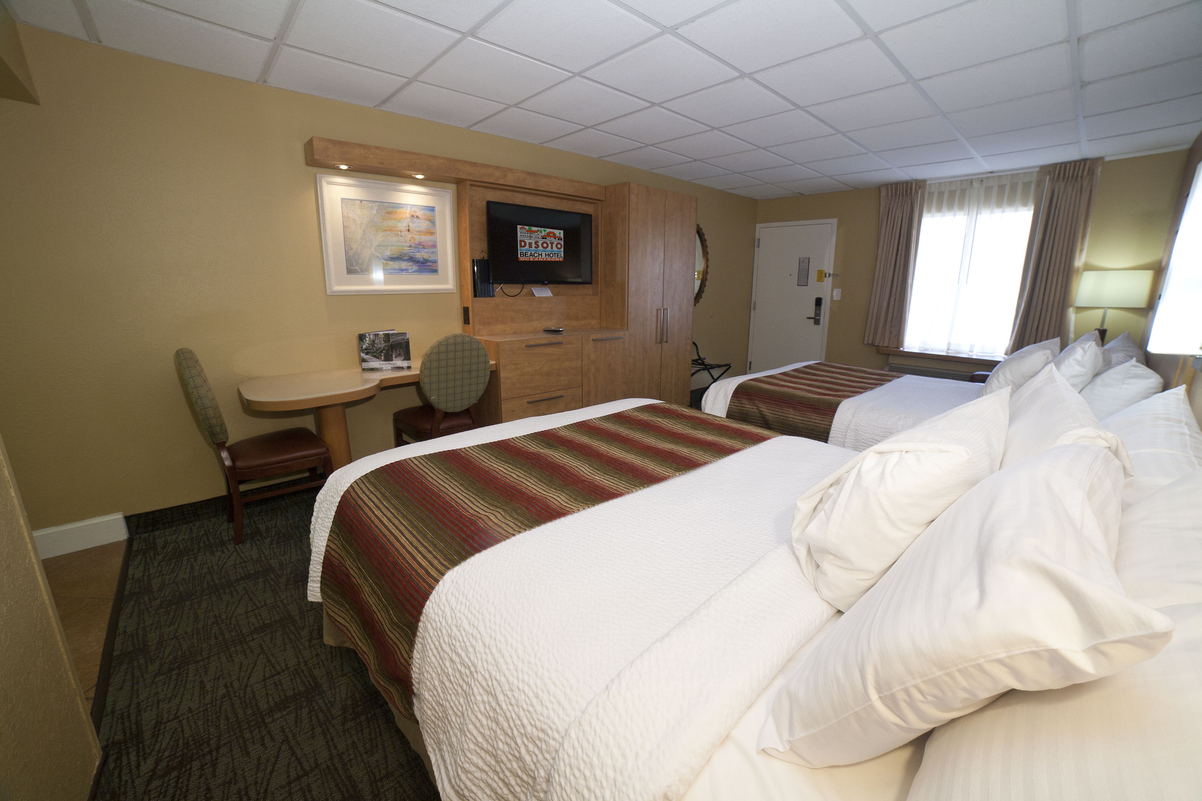 A hotel room with two beds, a desk, a chair, a television, and a door.