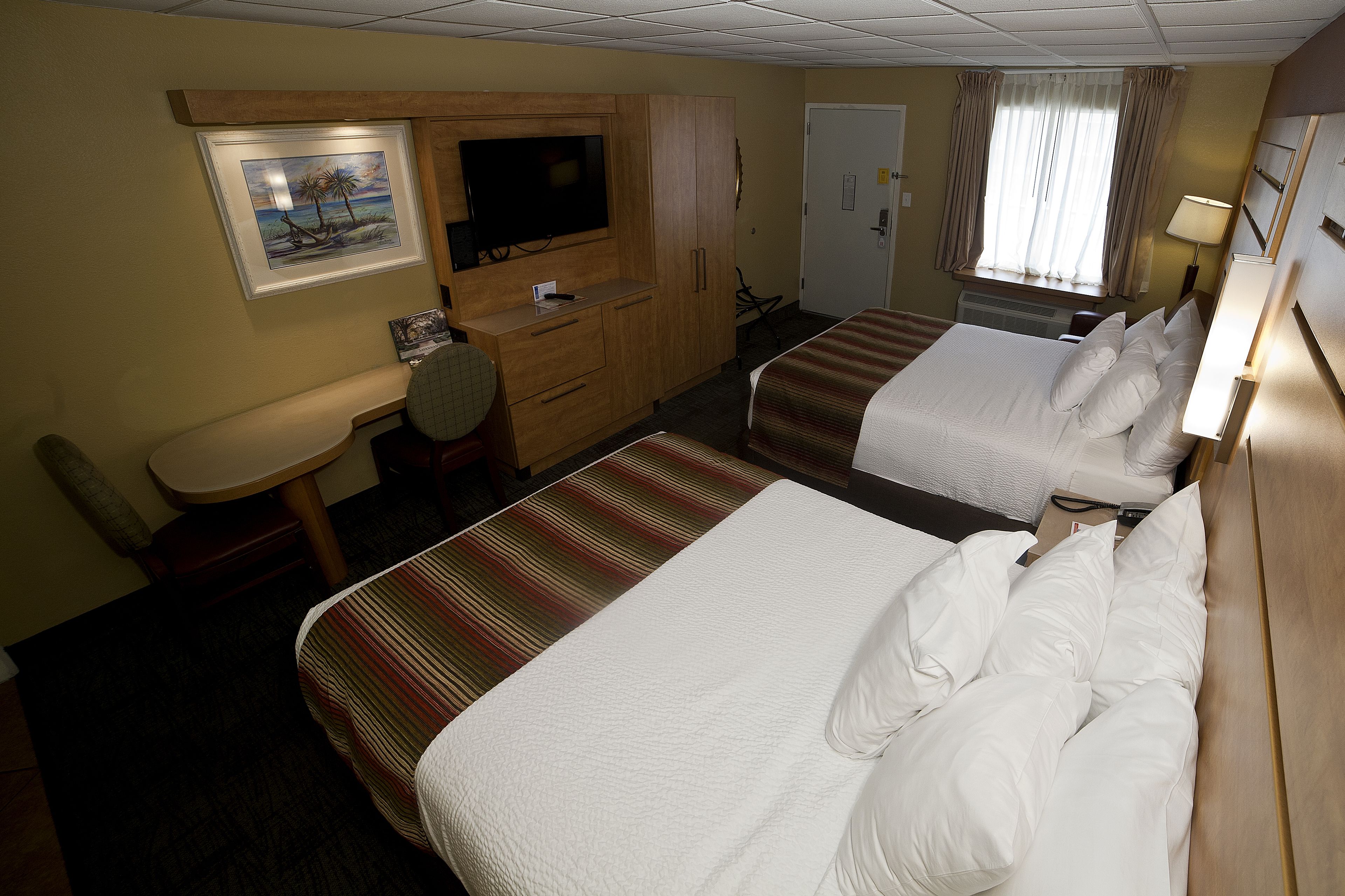 A hotel room with two beds, a desk, a television, and a window with curtains.