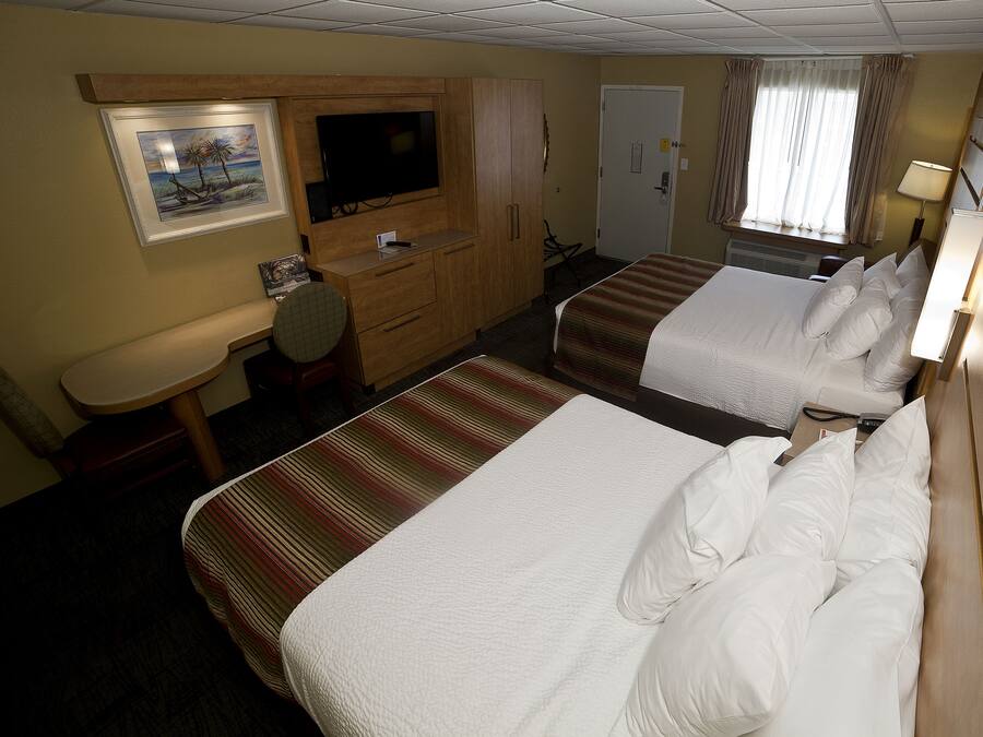 A hotel room with two beds, a desk, a television, and a window with curtains.