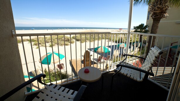 Un balcon avec vue sur la plage, des meubles d’extérieur et un palmier.