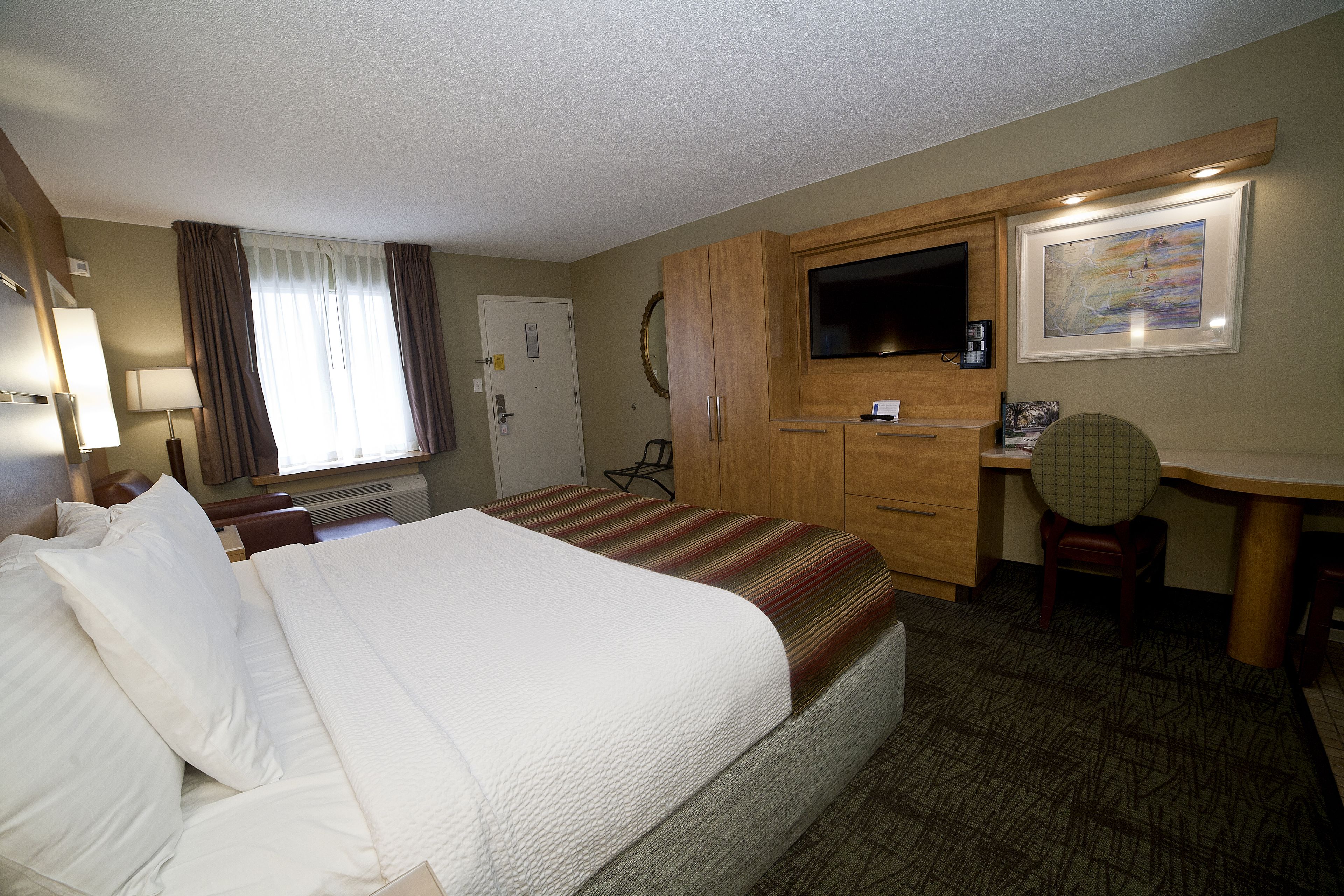 A hotel room with a bed, a desk, a chair, a television, and a framed picture on the wall.
