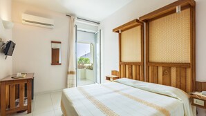 A hotel room with a bed, a desk, a mirror, an air conditioner, and a view of the outside. - Hotel Miramare (Dorgali)
