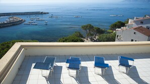 A terrace with blue chairs and a view of the sea and boats. - Hotel Miramare (Dorgali)